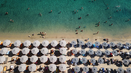Aerial drone, bird's eye view photo of famous crowded full of sun beds turquoise colour sandy beach of Ornos, Mykonos island, Cyclades, Greece