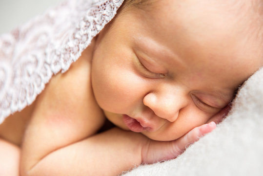 Newborn baby sleeping in white lace on light background