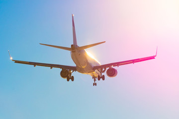 Passenger airplane flies near the sun glare with a color rainbow gradient on landing.