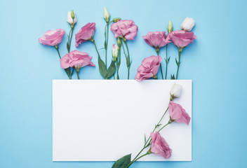Flowers composition. Wreath made of pink flowers with white paper card on blue background. Flat lay, top view, copy space