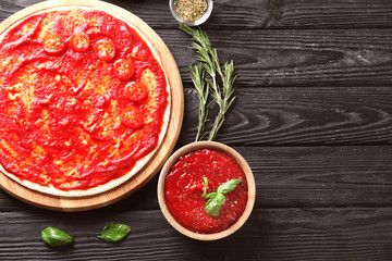 Composition with pizza dough and tasty tomato sauce on wooden background