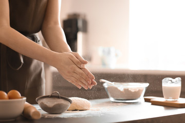 Baker sprinkling flour on dough at table