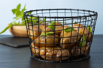 Baked potatoes in a black basket. Basil in the vase. The background is light blue. Copy space. Horizontal shot.