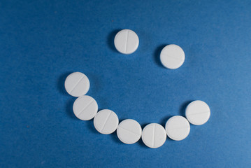 Happy smile made from white pills on blue background