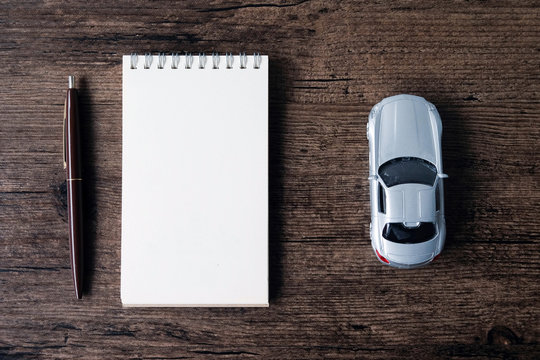Top view image of blank page notebook ,pen and small car model on the wooden table..