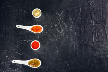 Composition with different sauces on black textured background, top view