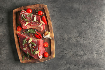 Wooden board with raw meat and vegetables on grey background, top view