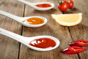 Ceramic spoons with different sauces and ingredients on wooden background, closeup