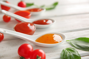 Ceramic spoons and bowls with different sauces on table, closeup
