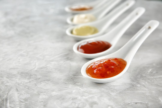 Ceramic spoons with different sauces on grey background