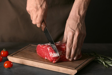 Man cutting fresh raw meat on wooden board