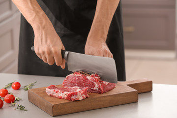Man cutting fresh raw meat on wooden board in kitchen