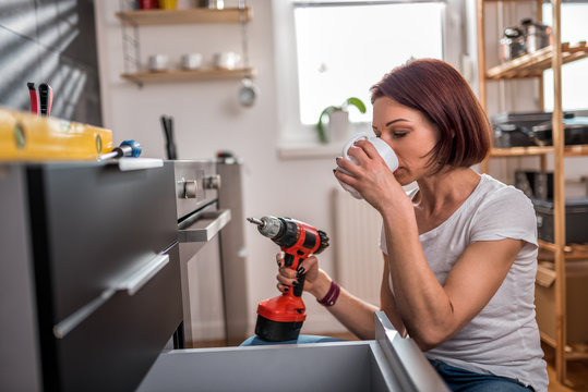 Woman drinking coffee while building a kitchen cabinet