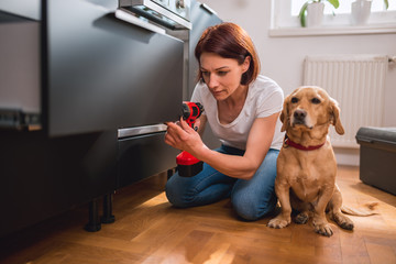 Woman with dog building kitchen and using a cordless drill