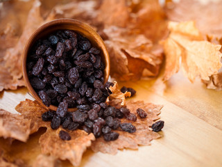 Black raisins in a wooden bowl. On dry leaf and brown wooden background..