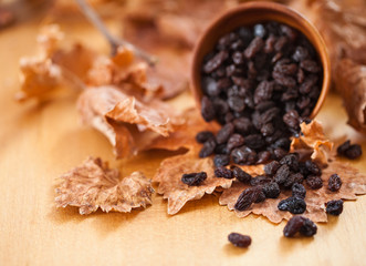 Black raisins in a wooden bowl. On dry leaf and brown wooden background.