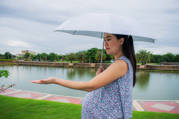 Pregnant woman holding an umbrella at the park in the drizzly day.