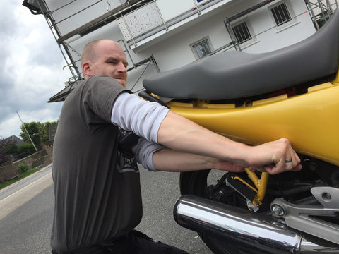 junger Mann mit Glatze repariert ein Motorrad