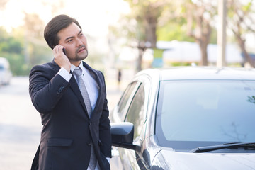 Handsome businessman using a mobile phone lerning on his car