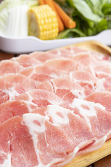 sliced raw pork on wooden plate with vegetables