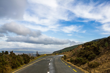 Obraz premium Amazing view from road leading into curve and down to valley. Sun and clouds, rain and wind. Typical scene from Ireland. Very changeable weather. Beautiful country. Popular travel destination.