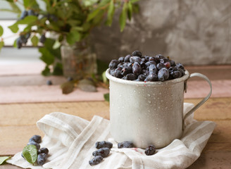 Honeysuckle berry in metal cup with green leaves on a wooden table