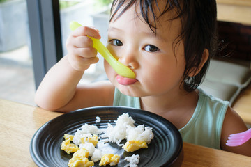 A child is trying to eat with spoon and fork by herself. Baby eating.