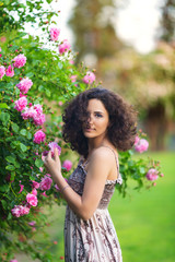 Naklejka premium Portrait of a smiling young brunette Caucasian beautiful woman near rose bush, vertical, waist up