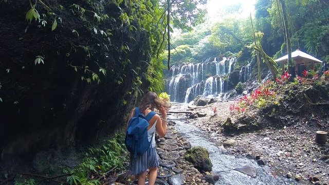 Slow motion shot from behind of a curly girl walking to a waterfall