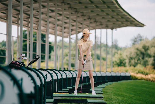 Woman In Yellow Cap And Polo Playing Golf At Golf Course