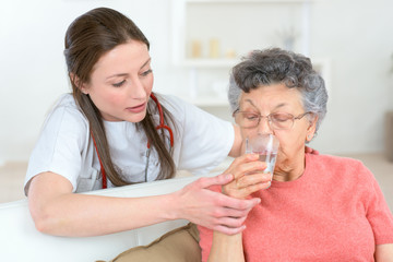 doctor giving sick senior woman a glass of water