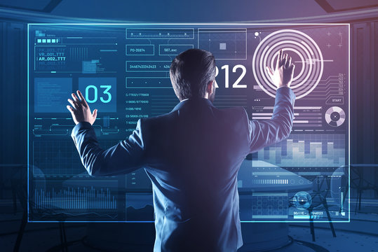 Touching the icons. Clever elegant database administrator carefully touching the icons on a transparent screen while working with a futuristic device