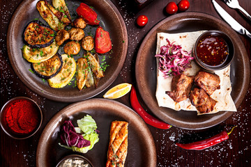 Aassorted traditional Georgian food on a wooden background and rustic plates. Top view of skewers, grilled vegetables, grilled salmon with herbs and spices.
