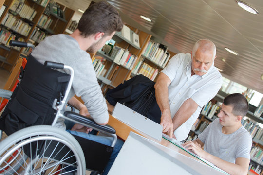 Man with students in library, one in wheelchair