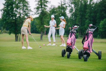 Obraz premium selective focus of golf gear, woman in cap with golf club and friends standing near by at golf course