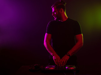 DJ at work mixing sound on her decks at a party or night club with colourful smoke light background