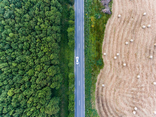 Aerial View Of car driving on Road through  Forest And Agriculture harvest field of hay bales in rural Ireland during summer