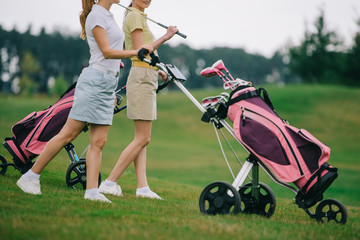 Obraz premium partial view of female golf players in polos walking on golf course