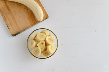 A part of the peeled banana on the cutting board and fresh ripe organic sliced bananas in a glass bowl.