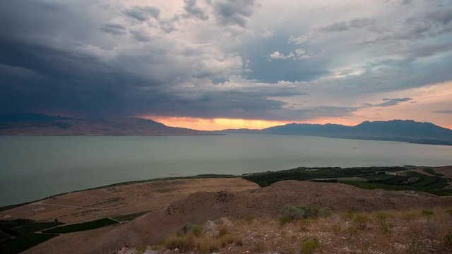 Dark storm clouds rolling through valley over Utah Lake with lightning strike at sunset.