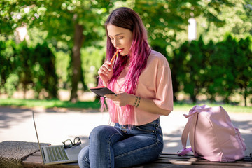 Woman writing in a notebook sitting on a wooden bench in the park. Girl working outdoors on portable computer, copy space.