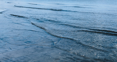 Small waves reaching seashore. Waves rolling in the beach. Calm on the river or the sea. Flood.