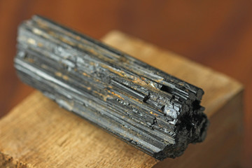 Black tourmaline stone on a background of natural wood American black walnut. Mineral collection...