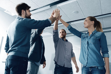 Rely on me. Cheerful young group of people standing in the office and giving high five while working together