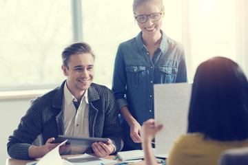Present your idea. Smiling man holding his tablet and sitting opposite his colleague while looking at presentation