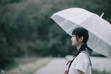 Portrait of Asian school girl walking with umbrella at  nature walkway on raining