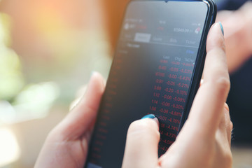 Close up on woman hand holding smartphone trading stock and data in coffee shop background business concept