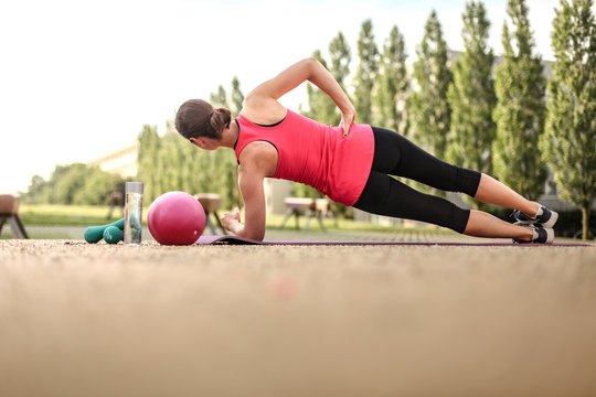 sporty and strong woman making planks infront of a laptop while watching online Fitness program on a mat in the park