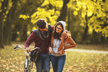 Young couple riding bicycle outdoors at autumn at the park.
