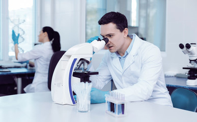 Professional biologist. Pleasant nice handsome man sitting in the lab and using a microscope while...